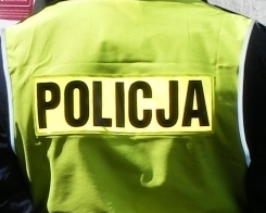 Policjant stojący tyłem, ubrany w kamizelkę odblaskową z napisem Policja