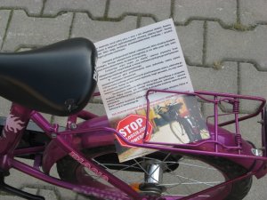 Zdjęcie kolorowe. Rower dziecięcy. Na bagażniku umieszczona ulotka informacyjne z hasłem &quot;Stop złodziejom rowerów!&quot;