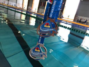 Zdjęcie kolorowe. Medale Letnich Otwartych Mistrzostwach Polski w Pływaniu - Masters na tle basenu pływckiego.
