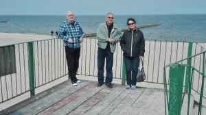 Zdjęcie kolorowe. Troje seniorów pozujących do zdjęcia na tle morza.