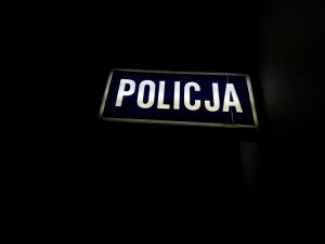 Zdjęcie kolorowe. Prostokątny neon koloru granatowego z białym napisem Policja.
