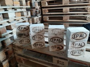 Zdjęcie kolorowe. Stos palet na którym położone są drewniane klocki z wypalonym logo EPAL