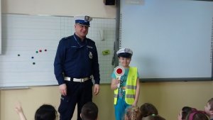 zdjęcie kolorowe na zdjęciu policjant ruchu drogowego razem z uczniem w czapce policyjnej