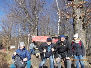 Zdjęcie kolorowe. Grupa osób pozująca do zdjęcia. Las i tablica koloru czerwonego z napisem &quot;Ślężański Park Krajobrazowy&quot;.