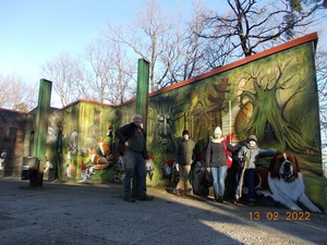 Zdjęcie kolorowe. Cztery osoby pozujące do zdjęcia przy ścianie z namalowanym graffiti na którym umieszczony został las, krasnale oraz zwierzęta.