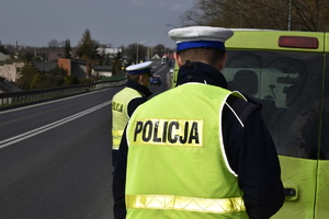 Zdjęcie kolorowe. Policjanci z ruchu drogowego w umundurowaniu służbowym i odblaskowych kamizelach z napisem &quot;Policja&quot; kontrolują pojazd typu bus.