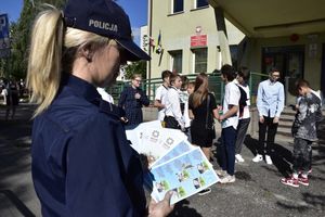 zdjęcie numer siedem, kolorowe, na zdjęciu policjant rozdający ulotki informacyjne i odblaski dzieciom idącym na rozpoczęcie roku szkolnego