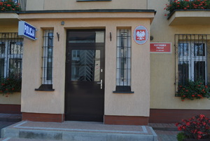 Zdjęcie kolorowe. Front elewacji w środkowej części drzwi wejściowe. Po prawej stronie czerwona tablica z białym napisem Posterunek Policji w Liskowie. Nad drzwiami biały napis Policja na granatowym tle.