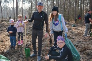 Zdjęcie kolorowe. Las. Mężczyzna z grupą dzieci uczestniczący w akcji sadzenia drzew w lesie.