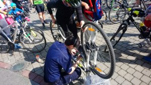 Zdjęcie kolorowe. Policjantka w umundurowaniu służbowym znakuje rower jednego z uczestników Rodzinnego Rajdu Rowerowego &quot;Z przedszkolakiem na rowerze&quot;.