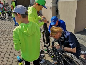 Zdjęcie kolorowe. Policjantka z Zespołu Profilaktyki Społecznej znakuje rower jednego z uczestników  Rodzinnego Rajdu Rowerowego &quot;Z przedszkolakiem na rowerze&quot;.