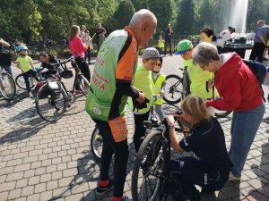 Zdjęcie kolorowe. Policjantka w umundurowaniu służbowym znakuje rower jednego z uczestników Rodzinnego Rajdu Rowerowego &quot;Z przedszkolakiem na rowerze&quot;.