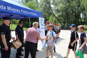 Pierwsze zdjęcie kolorowe, przedstawia rozstrzygnięcie tegorocznej edycji Rajdu Urwisa w Parku Przyjaźni, na nim uczestnicy oraz organizatorzy przedsięwzięcia- przedstawiciele Komendy Miejskiej Policji w Kaliszu , Wydziału Spraw Społecznych oraz Mieszkaniowych Urzędu Miejskiego w Kaliszu oraz harcerze ZHP w Kaliszu.
Drugie zdjęcie kolorowe, na  nim uczestnicy rajdu urwisa biorący udział w konkurencji.
Trzecie zdjęcie kolorowe, na nim trzech chłopców wykonujących zadanie podczas Rajdu Urwisa. 
Czwarte zdjęcie kolorowe, na nim chłopiec trzymający w ręku wykonany rysunek.
Piąte zdjęcie kolorowe, na nim I Zastępca Komendanta Miejskiego Policji w Kaliszu mł. insp. Tadeusz Królikowski, Zastępca Naczelnika Wydziału Prewencji i Profilaktyki Społecznej KMP w Kaliszu podkom. Witold Woźniak oraz Zastępca Naczelnika Wydziału Spraw Społecznych i Mieszkaniowych Urzędu Miejskiego w Kaliszu Janusz Sibiński oraz trzech chłopców którzy w ręku trzymają upominki.
Szóste zdjęcie kolorowe, na nim Zastępca Naczelnika Wydziału Spraw Społecznych i Mieszkaniowych Urzędu Miejskiego w Kaliszu Janusz Sibiński wręcza nagrodę drużynie biorącej udział w rajdzie urwisa oraz I Zastępca Komendanta Miejskiego Policji w Kaliszu mł. insp. Tadeusz Królikowski i Zastępca Naczelnika Wydziału Prewencji i Profilaktyki Społecznej KMP w Kaliszu podkom. Witold Woźniak.
Siódme zdjęcie kolorowe, na nim przedstawiciele Komendy Miejskiej Policji w Kaliszu,  Urzędu Miejskiego w Kaliszu oraz uczestnicy Rajdu Urwisa trzymający w ręku otrzymane upominki.