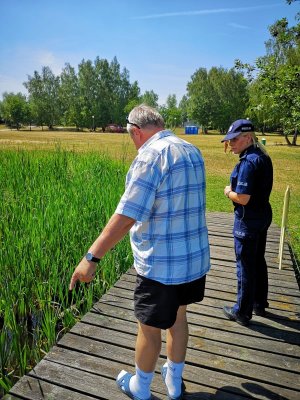 Zdjęcie kolorowe.Stojący na pomoście nad akwenem wodnym policjantka  oraz przedstawiciel WOPR podczas kontroli niestrzeżonych kąpielisk