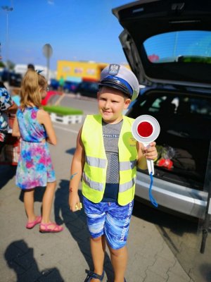 zdjęcie pierwsze kolorowe, na nim chłopiec ubrany w odblaskową kamizelkę policyjną, czapkę policyjną, w prawej dłoni trzyma tarcze do zatrzymywania pojazdów  a w lewej tarcze ochronną
drugie zdjęcie kolorowe, na nim chłopiec ubrany w kamizelkę odblaskową, czapkę policjanta, w ręku trzyma tarcze do zatrzymywania pojazdów, w tle radiowóz  policyjny
trzecie zdjęcie kolorowe, policjantka w umundurowaniu służbowym rozdaje elementy odblaskowe podczas pikniku ,,Bezpieczny powrót do szkoły&#039;&#039;
czwarte zdjęcie kolorowe, na nim dziewczynka ubrana w kamizelkę odblaskową, czapkę policyjną w ręku trzyma tarcze służącą do zatrzymywania pojazdów.