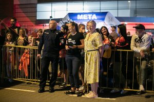 Zdjęcie kolorowe. Mł. insp. Witold Goździewski  Zastępca Komendanta Miejskiego Policji w Kaliszu w umundurowaniu służbowym w towarzystwie pracowników Ośrodka Sportu Rehabilitacji i Rekreacji w Kaliszu. W tle kibice stojący za barierkami ochronnymi.