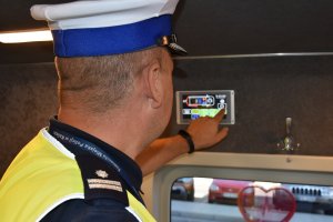 Zdjecię kolorowe. Policjant ruchu drogowego stający tyłem wewnątrz radiowozu volkswageny Crafter. Policjant włącza tablet, którym można sterować urządzeniami zamontowanymi w pojeździe.