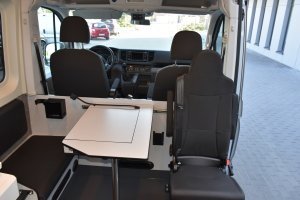 Zdjęcie kolorowe. Wnętrze radiowozu oznakowanego pojazdu Volkswagen Crafter. Stolik i trzy fotele.