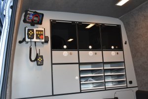 Zdjęcie kolorowe. Wnętrze radiowozu Volkswagen Crafter. Półki na druki.  Z prawej strony zawieszony tablet i pilot służący do obsługi zamontowanych w pojeździe urządzeń.