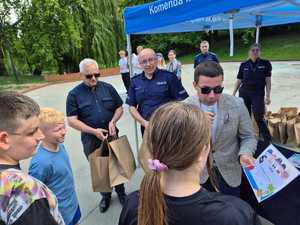 Zdjęcie kolorowe. Uczestnicy &quot;Biegu Urwisa&quot; odbierają dyplom z rąk Wiceprezydenta miasta Kalisza. Obok Zastępca Komendanta Miejskiego Policji w Kaliszu w umundurowaniu służbowym, oraz Zastępca Naczelnika Spraw Społecznych i Mieszkaniowych. W tle policjanci.