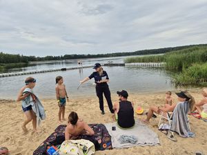 Pierwsze zdjęcie kolorowe , na nim osoby wypoczywające nad wodą oraz policjantka w tle rozmawiająca z dzieckiem.
Drugie zdjęcie kolorowe na nim policjantka rozmawiająca z osobami przebywającymi nad wodą.
Trzecie zdjęcie kolorowe, na nim policjantka z dziećmi na plaży.
Czwarte zdjęcie kolorowe, na nim policjantka z dziećmi na plaży udzielająca porad na temat bezpieczeństwa nad wodą.
Piąte zdjęcie kolorowe, przedstawia policjantkę wręczającą ulotkę ,,kręci mnie bezpieczeństwo nad wodą&#039;&#039; plażowiczom.
Szóste zdjęcie kolorowe na nim policjantka przekazuję ulotkę pani siedzącej na plaży przy zalewie Murowaniec.