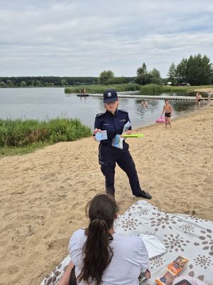 Pierwsze zdjęcie kolorowe , na nim osoby wypoczywające nad wodą oraz policjantka w tle rozmawiająca z dzieckiem.
Drugie zdjęcie kolorowe na nim policjantka rozmawiająca z osobami przebywającymi nad wodą.
Trzecie zdjęcie kolorowe, na nim policjantka z dziećmi na plaży.
Czwarte zdjęcie kolorowe, na nim policjantka z dziećmi na plaży udzielająca porad na temat bezpieczeństwa nad wodą.
Piąte zdjęcie kolorowe, przedstawia policjantkę wręczającą ulotkę ,,kręci mnie bezpieczeństwo nad wodą&#039;&#039; plażowiczom.
Szóste zdjęcie kolorowe na nim policjantka przekazuję ulotkę pani siedzącej na plaży przy zalewie Murowaniec.