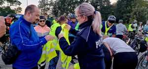 zdjęcie kolorowe, na zdjęciu uczestnicy rajdu rowerowego którym policjantka rozdaje kamizelki odblaskowe