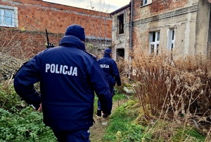 Zdjęcie kolorowe. Policjanci  w umundurowaniu służbowym podczas wchodzenia do pustostanu