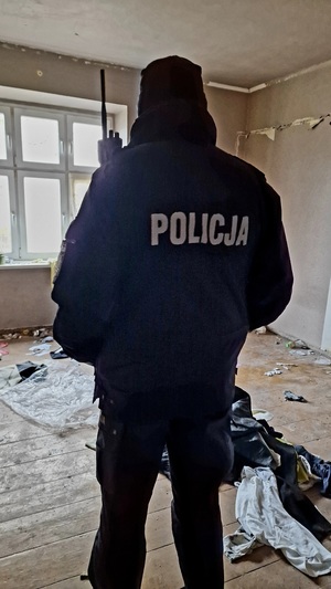 Policjant w umundurowaniu służbowym stojący w jednym z pomieszczeń pustostanu.