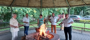 Zdjęcie kolorowe. Pięcioro uczestników spotkania integracynego podczas pieczenia kiełbasek nad ogniskiem.