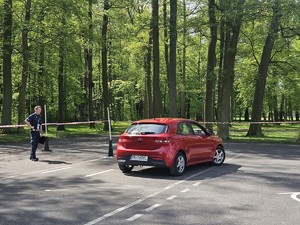Zdjęcie kolorowe. Policjant stojący na placu manewrowym obserwuje uczestnika  podczas eliminacji Ogólnopolskiego Młodzieżowego Turnieju Motoryzacyjnego, który pokonuje plac samochodem osobowym.