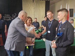 Zdjęcie Kolorowe. Kobieta oraz mężczyzna wręczają dyplom i puchar dwóm uczestnikom eliminacji Ogólnopolskiego Młodzieżowego Turnieju Motoryzacyjnego