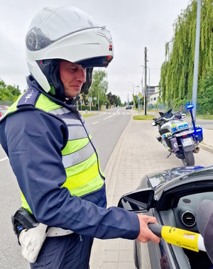 Zdjęcie kolorowe. Policjant w umundurowaniu służbowym (motocyklista) sprawdza stan trzeźwości zatrzymanego kierowcy.