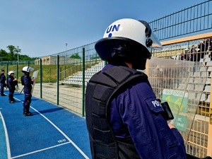 Zdjęcie kolorowe. Policjant w umundurowaniu ćwiczebnym z białym hełmem ochronnym na tle pustych trybun stadionu miejskiego.