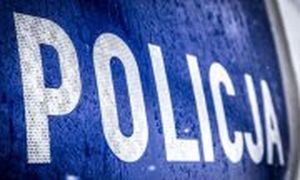 Zdjęcie kolorowe. Maska policyjnego radiowozu. Szary napis POLICJA na niebieskim tle.
