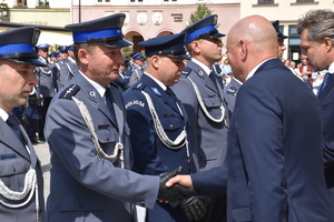 Zdjęcie kolorowe. Rząd policjantów stojący podczas uroczystości. Jeden z policjantów przyjmuje gratulacje z rąk Przewodniczącego Rady Miasta Kalisza