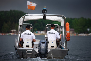 Zdjęcie kolorowe. Policjanci odwróceni tyłem na łodzi, patrolują rejon akwenu.