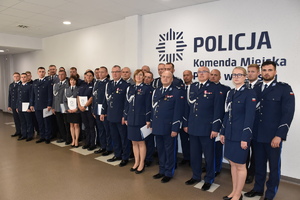 Zdjęcie kolorowe. Grupa policjantów ubrana w mundury koloru granatowego, pozuje do wspólnego zdjęcia. Z tyłu na ścianie częściowo widoczny napis Policja Komenda Miejska Policji w Kaliszu