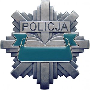 Grafika kolorowa. Ośmioramienna policyjna gwiazda w kolorze szarym z zieloną wstęgo w środkowej części.
