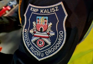 Zdjęcie kolorowe. Ramię policjanta w kurtce służbowej z logo Wydziału Ruchu Drogowego KMP Kalisz.