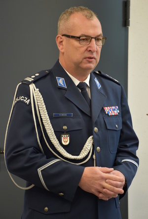 Zdjęcie kolorowe. Policjant w umundurowaniu wyjściowym ze sznurem.