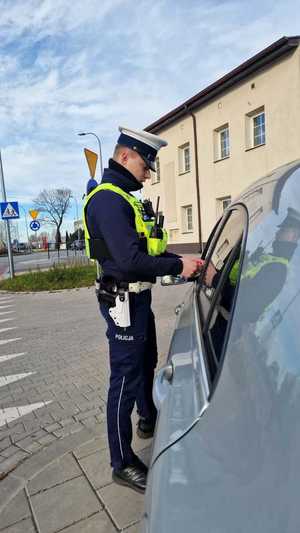 Zdjęcie kolorowe. Policjant ruchu drogowego. Stojący obok pojazdu zatrzymanego do kontroli drogowej.