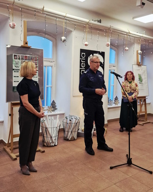 Zdjęcie kolorowe. Policjant stojący przed mikrofonem, obok stoją organizatorzy konkursu "Wolność bez nałogów".