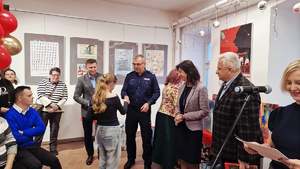 Zdjęcie kolorowe. Nastolatka odbiera gratulacje od policjanta. Stojący w sali przyglądają się wręczeniu nagrody.