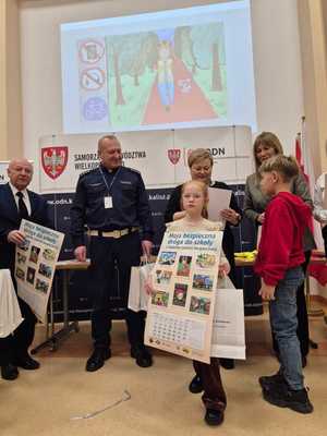 Zdjęcie kolorowe. Organizatorzy konkursu - Moja bezpieczna droga do szkoły - w kasku zawsze bezpieczniej, wręczją nagrody uczestniczce konkursu.