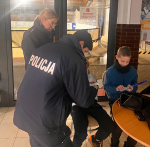 Zdjęcie kolorowe. Policjantki rozdają dzieciom ulotki i elementy odblaskowe.