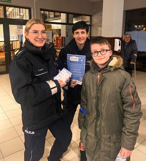 Zdjęcie kolorowe. Dwie policjantki pozują do zdjęcia z dzieckiem któremu wręczono ulotkę z konkursem Zimowy Dekalog.