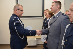 Zdjęcie kolorowe. Komendant Miejski Policji w Kaliszu wręcza akt minowania i gratuluje uściskiem dłoni awansowanemu funkcjonariuszowi.