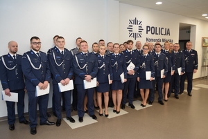 Zdjęcie kolorowe. Policjanci w umundurowaniu wyjściowym pozują do zdjęcia pod ścianą z napisem Komenda Miejska Policji w Kaliszu