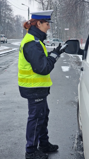 Zdjęcie kolorowe. Policjantka stoi przy drzwiach kierowcy busa, który został zatrzymany do kontroli drogowej.